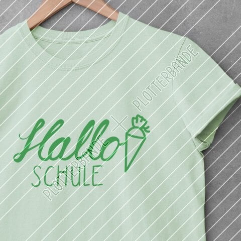 Ein grünes T-Shirt liegt auf einer Betonfläche. Darauf gedruckt ist das Hallo Schule-Design der Plotterbande.
