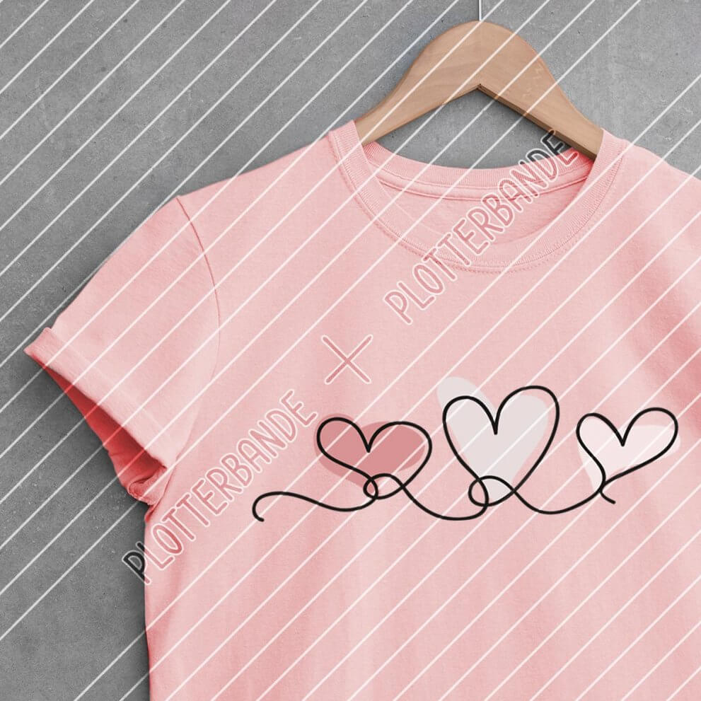 Ein pinkes T-Shirt mit dem Plotterbande-Design "Herzenslinie" liegt auf einer Betonoberfläche.