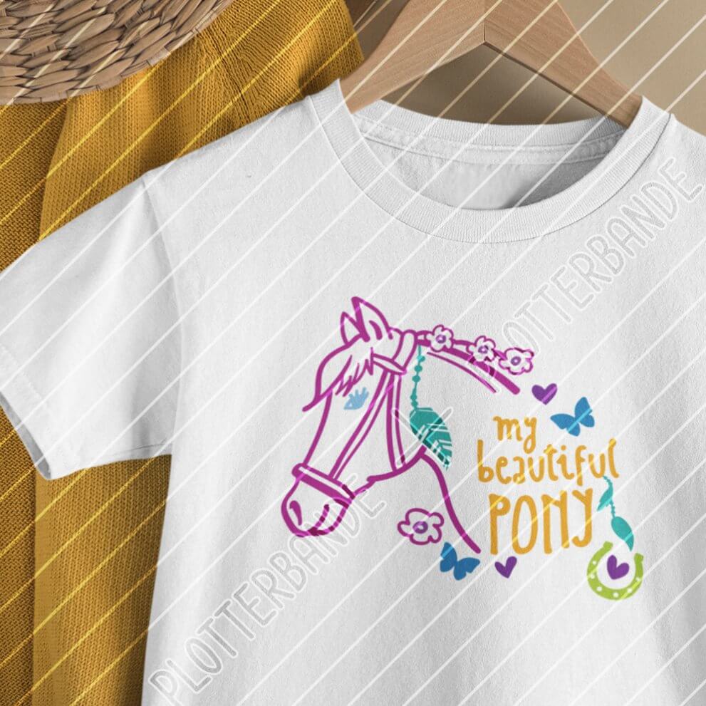 Das Bild zeigt ein weißes T-Shirt auf einem Kleiderbügel. Darauf ist das „My beautiful Pony“ Plottdesign der Plotterbande mit bunten Outlines.