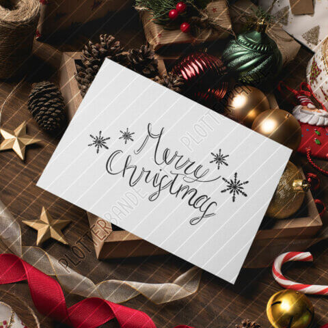 Ein weiße Karte liegt auf einem weihnachtlich dekorierten Tisch. Auf die Karte ist das Merry Christmas-Design der Plotterbande gedruckt.